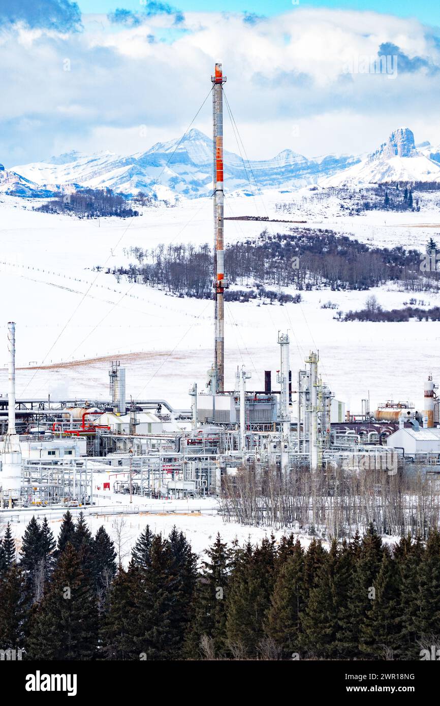Impianto di gas invernale con pila di bagliori che si affaccia sulle Montagne Rocciose canadesi e campi agricoli innevati ad ovest di Cochrane, Alberta Canada. Foto Stock