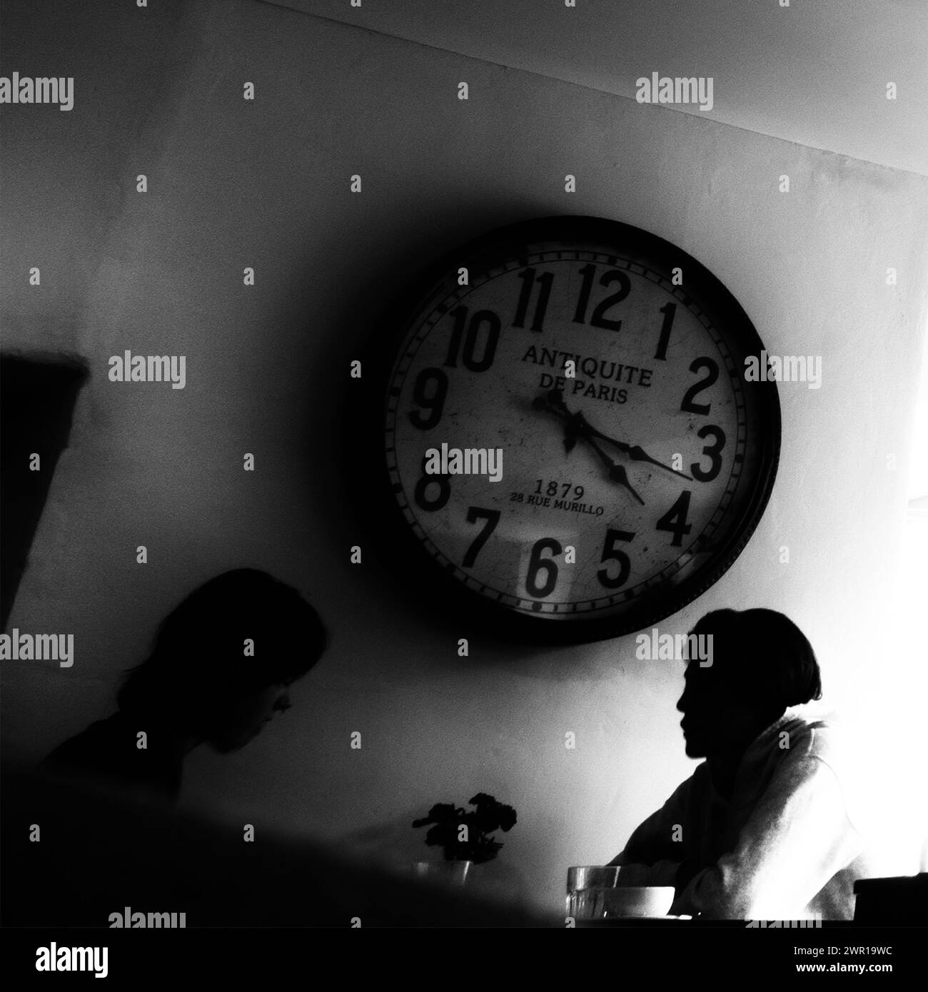 Immagine monocromatica all'interno di un bar con due persone che chiacchierano sul caffè con un grande orologio antico sul muro, Regno Unito Foto Stock