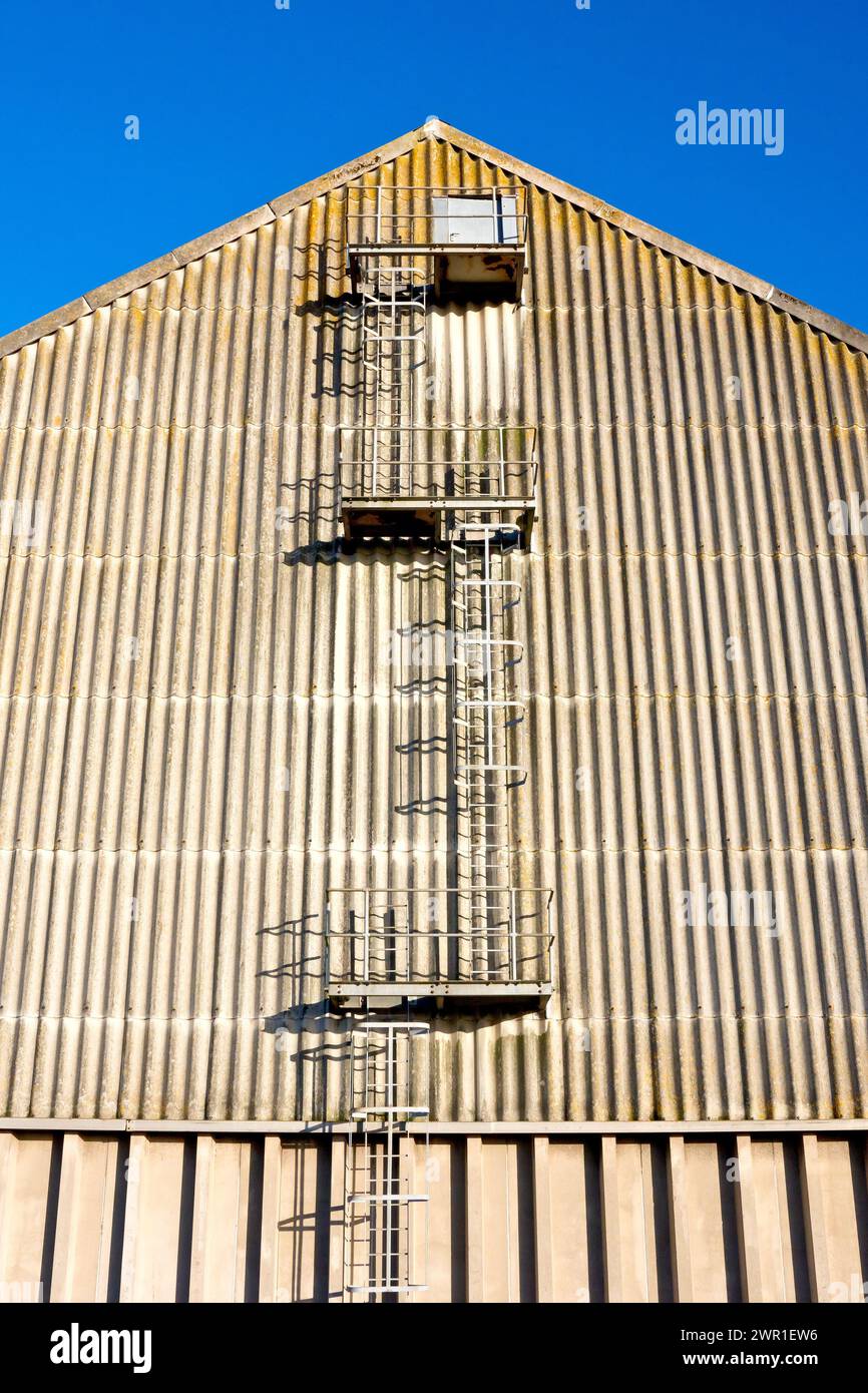 Una vista finale di un grande edificio in stile magazzino in una zona industriale con un set di scale protette sfalsate che salgono su una porta in cima. Foto Stock