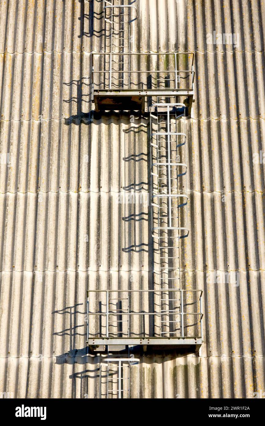 Vista di una serie di scale protette sfalsate che risalgono fino alla fine di un grande edificio in stile magazzino in una zona industriale. Foto Stock