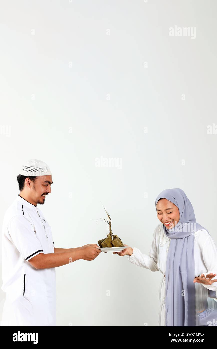 Due musulmani asiatici che tengono un piatto bianco con Ketupat per la celebrazione Eid al Fitr, isolato sul bianco Foto Stock
