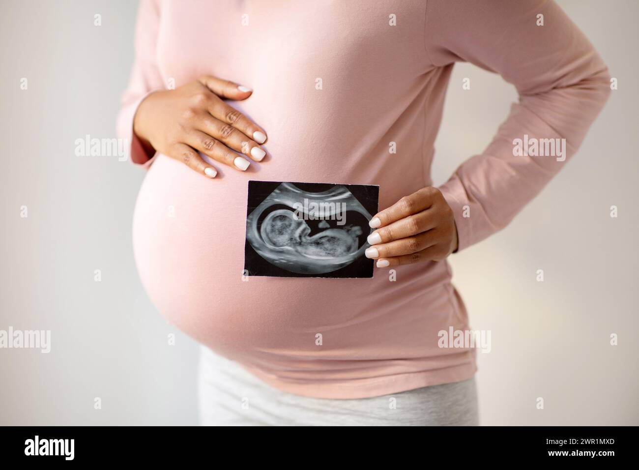 Donna incinta che mostra amorevolmente la sua foto ecografica e abbraccia dolcemente la pancia Foto Stock