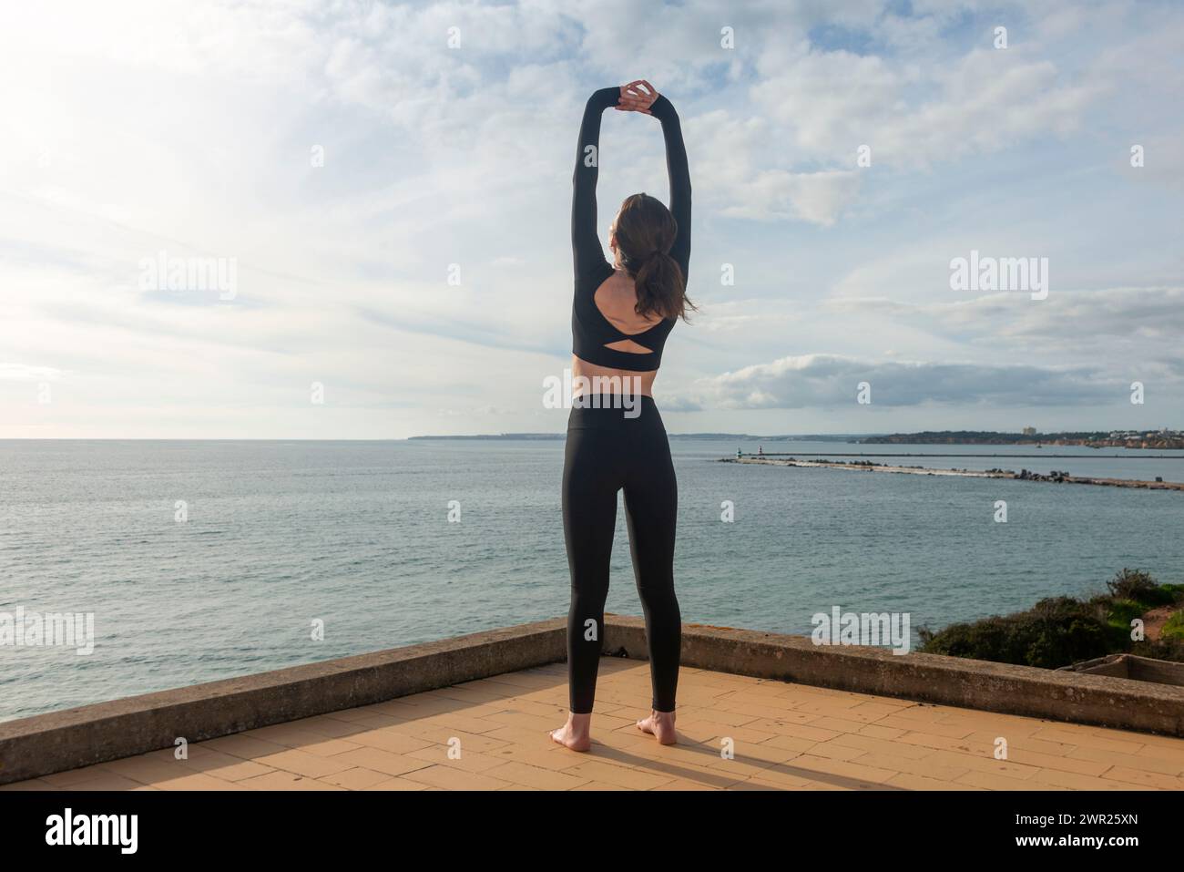 vista posteriore di una donna che si allunga, si allena in riva al mare Foto Stock