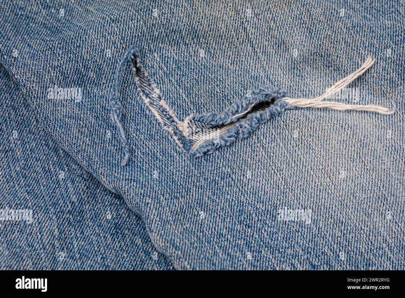 Lacerazione nei jeans in denim. Concetto di riparazione e cura dell'abbigliamento e dei pantaloni da lavoro in denim. Foto Stock