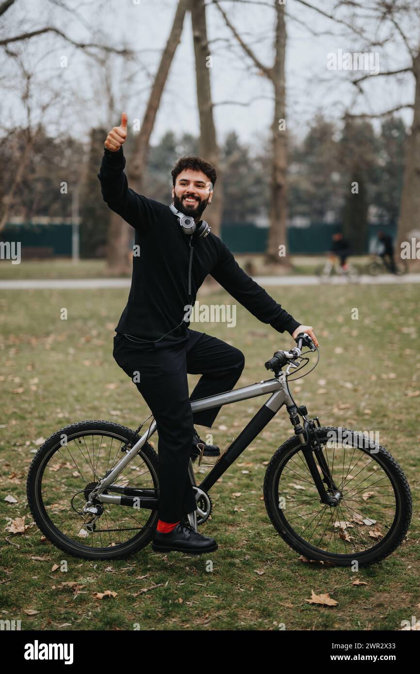 Un uomo d'affari sorridente in giro in bicicletta che regala un pollice nel parco. Foto Stock