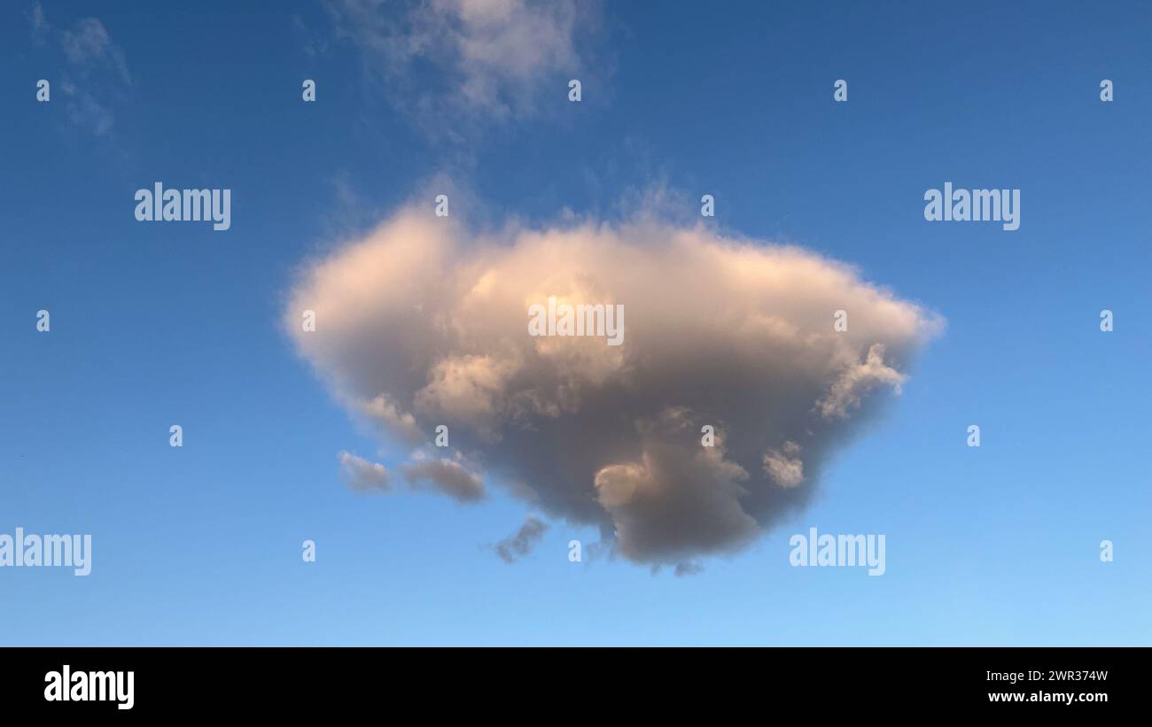 Nuvola di cumulus grigia solitaria al tramonto con cielo blu Foto Stock