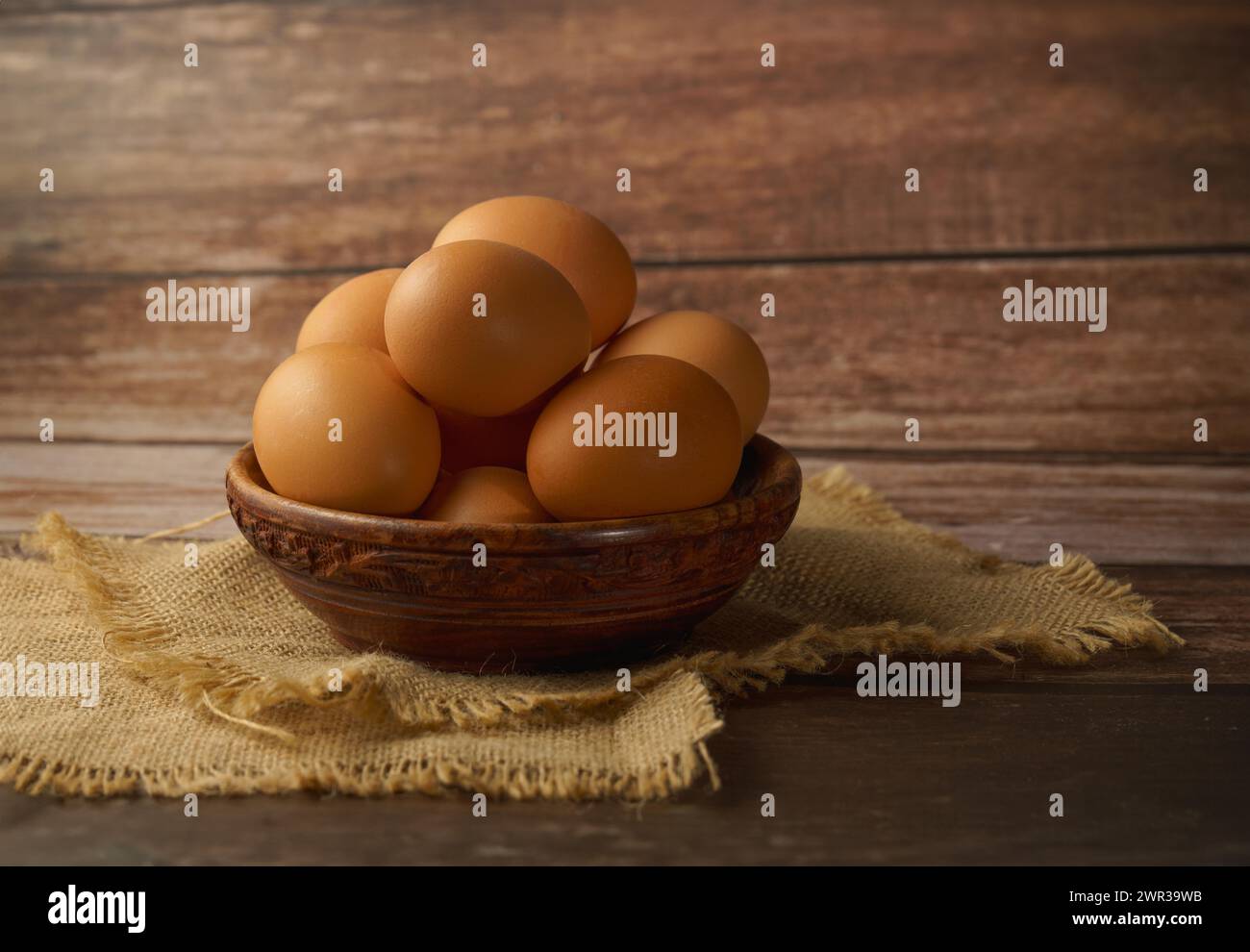 Uova fresche in una ciotola di legno su un telo di tela su un tavolo di legno Foto Stock