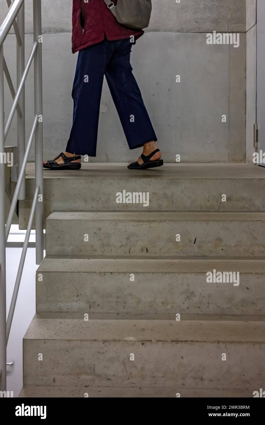 Una persona in jeans e sandali sale su una scala di cemento in un edificio Foto Stock