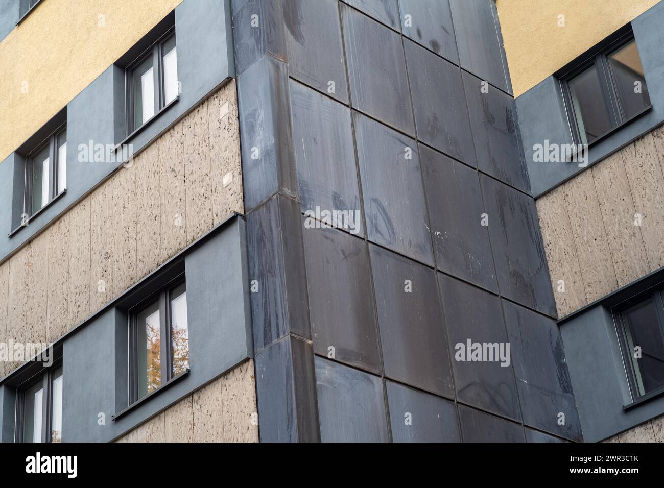 Pannelli scuri all'angolo dell'edificio contrastano con la facciata e le finestre di cemento di colore chiaro Foto Stock