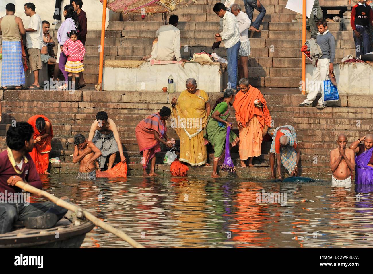 Le persone in abito tradizionale eseguono riti religiosi nell'acqua del fiume vicino a gradini di pietra, Varanasi, Uttar Pradesh, India Foto Stock