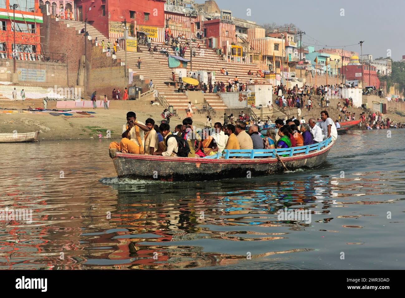 Barca piena di passeggeri su un fiume, città sullo sfondo, Varanasi, Uttar Pradesh, India Foto Stock