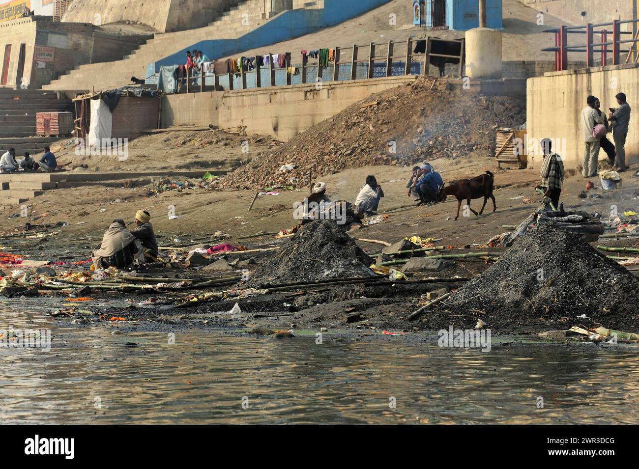 Riva del fiume con persone e animali, circondata da rifiuti e fumo, creando un'atmosfera nebulosa, Varanasi, Uttar Pradesh, India Foto Stock