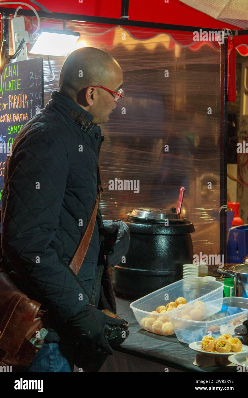 Comprare cibo da un venditore di cibo in una bancarella di mercato a Brick Lane a Londra Foto Stock