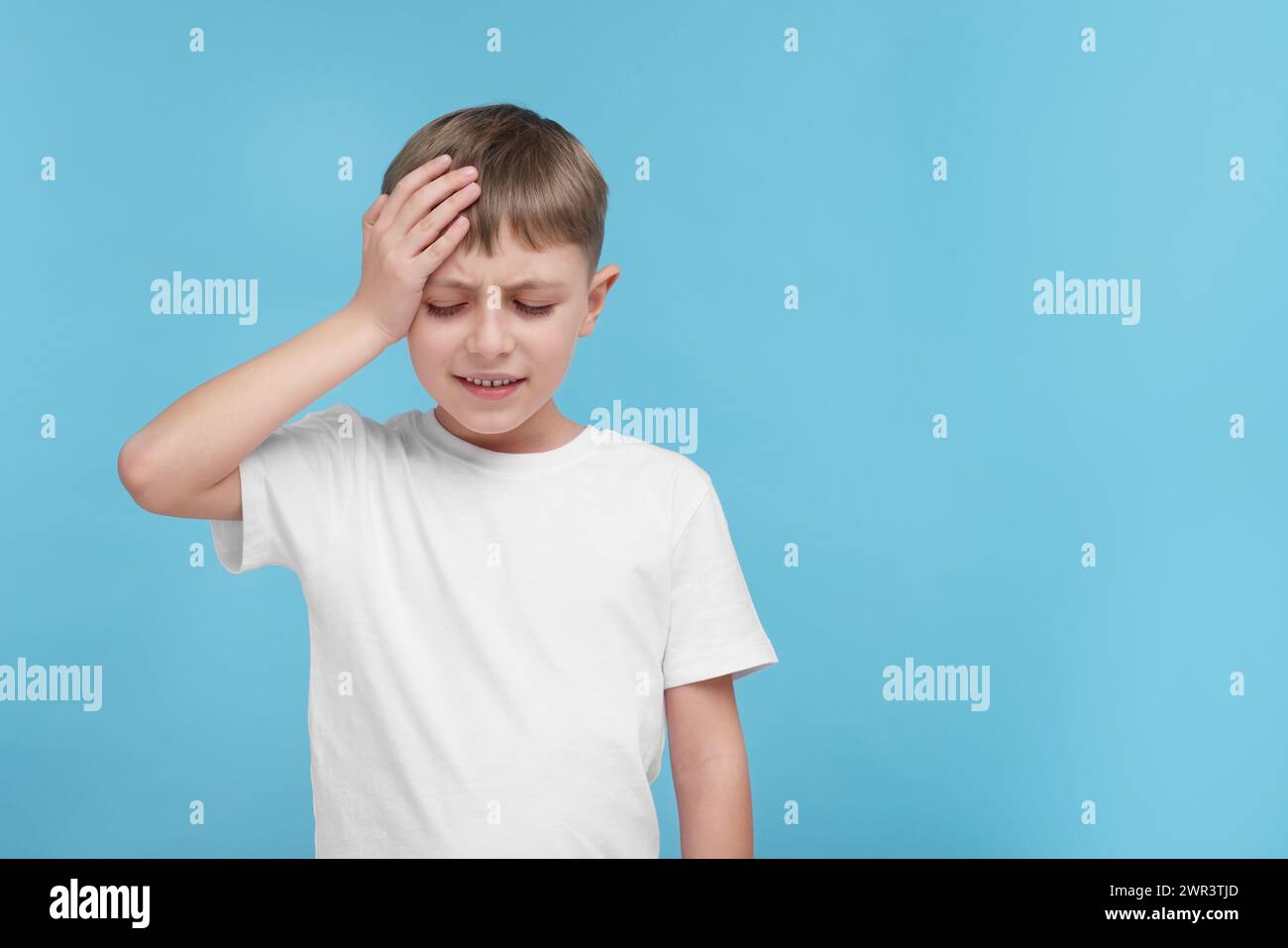 Bambino che soffre di mal di testa su sfondo azzurro, spazio per il testo Foto Stock