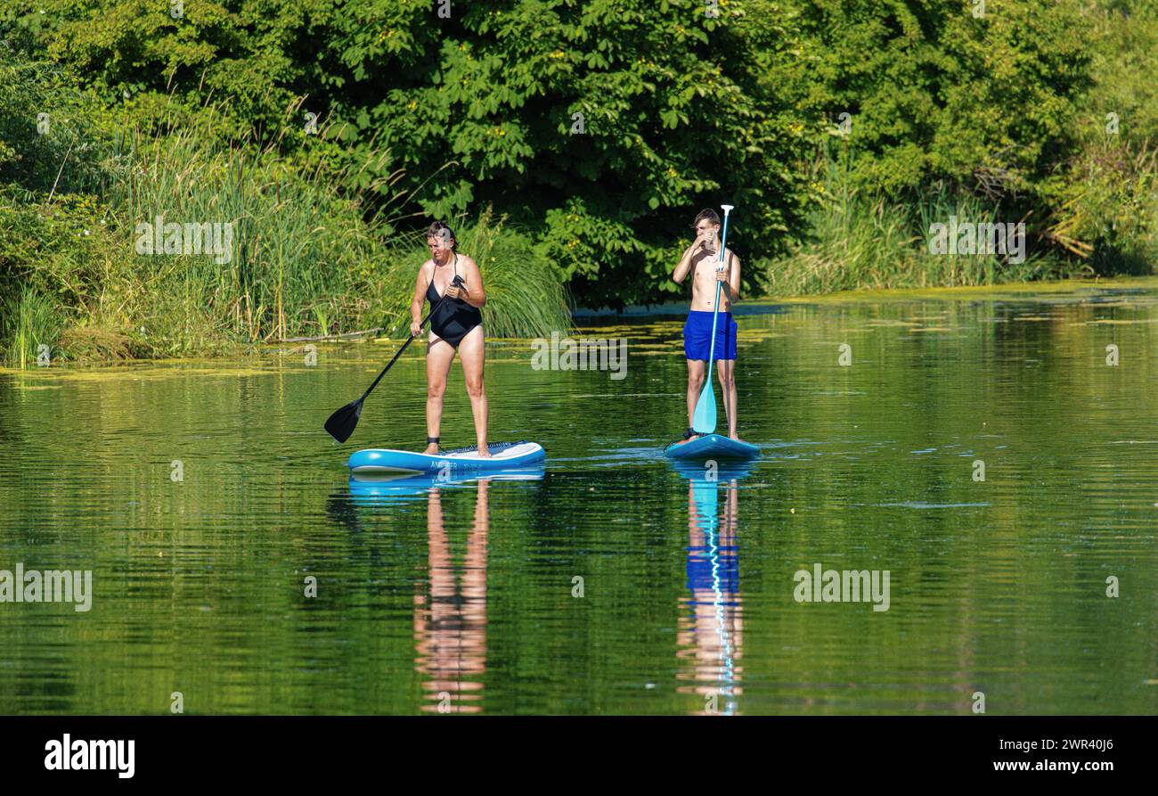 Zwei Personen vergnügen sich mit ihrem Stand Up Paddle auf dem Rhein. (Rheinau, Schweiz, 09.07.2023) Foto Stock