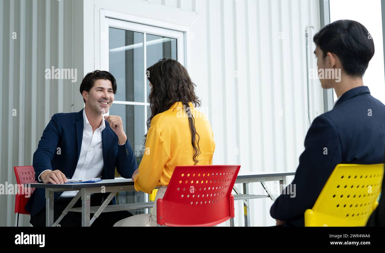 Tre persone sono sedute a un tavolo, con un uomo in costume e cravatta che sorride agli altri due Foto Stock