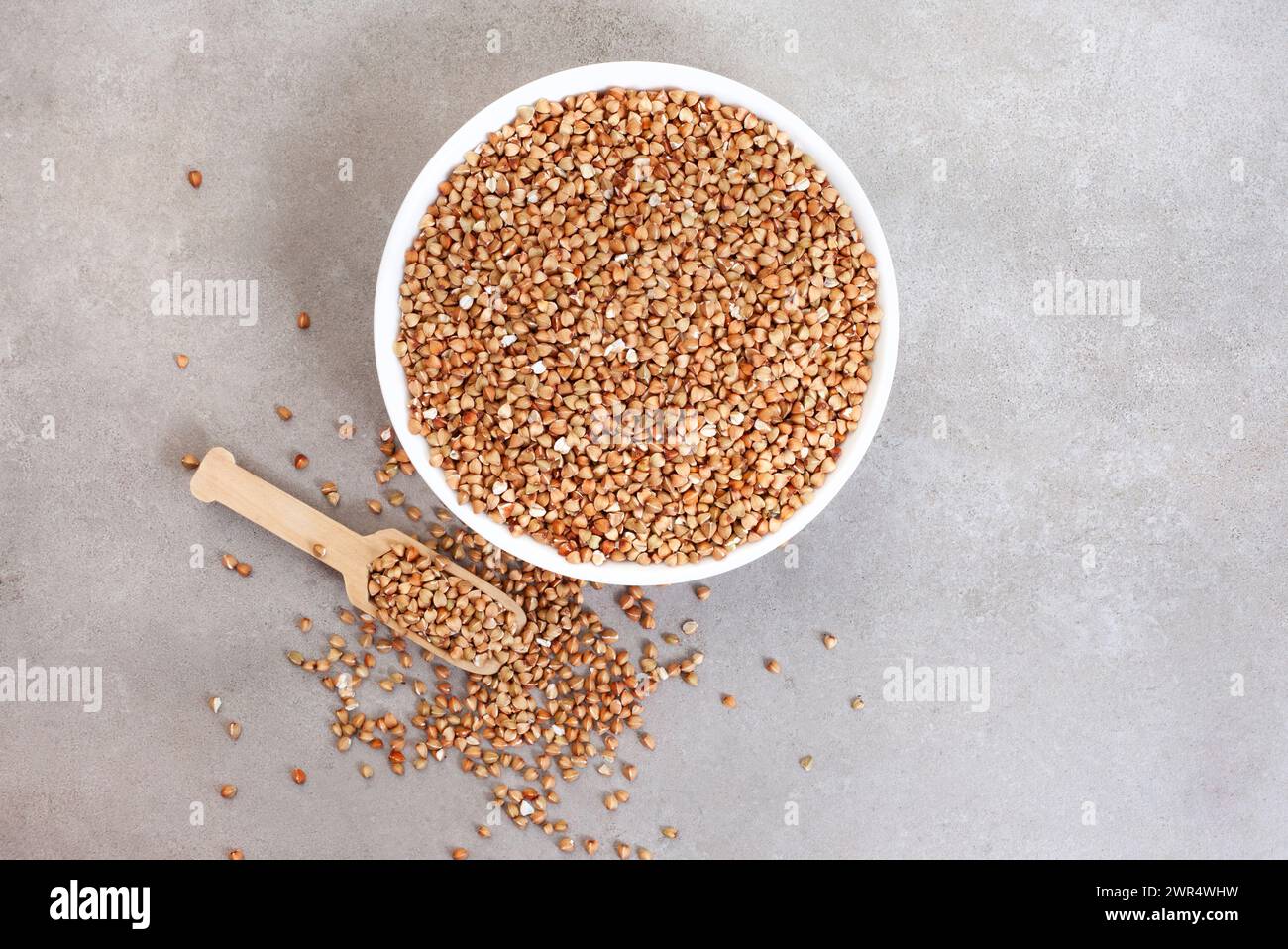 De il grano saraceno mondato in un recipiente con paletta su una superficie grigia a chiazze, vista dall'alto con spazio per copiare Foto Stock