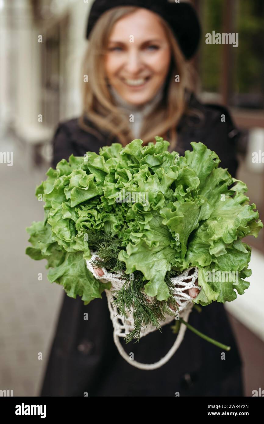 Una donna che tiene in mano un mucchio di lattuga fresca, mostrando le foglie verdi vivaci. Immagine verticale. Foto Stock