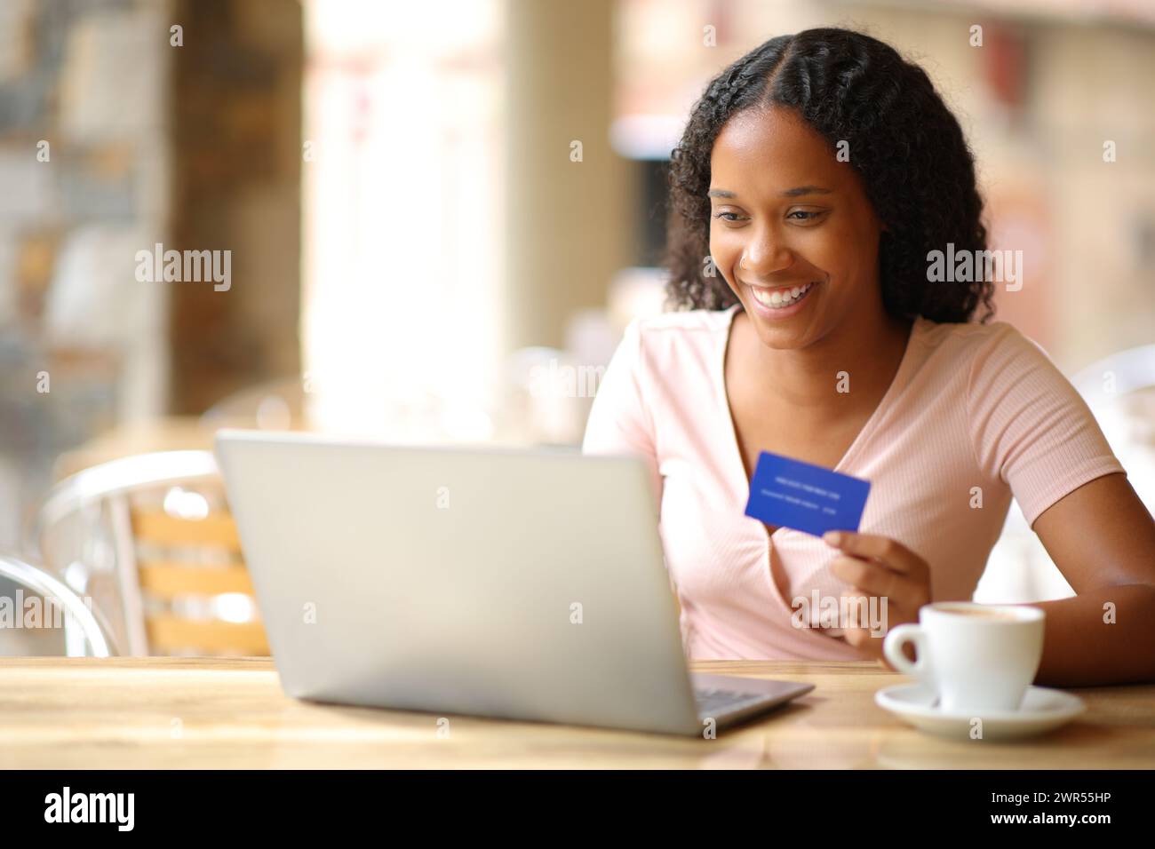 Acquirente online nero che paga online utilizzando un computer portatile e una carta di credito sulla terrazza di un ristorante Foto Stock