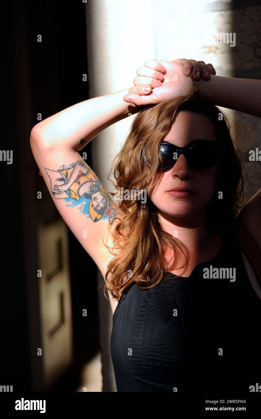 Young Pretty Girl con occhiali da sole e tatuaggi sul servizio fotografico di strada alla luce del tramonto Foto Stock