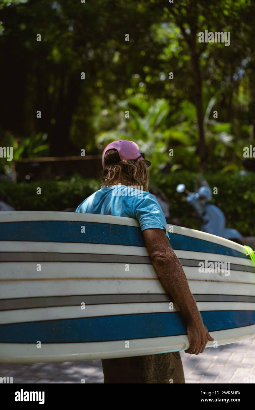 Uomo surfista con lunghi capelli sbiancati con una tavola da surf. Foto Stock