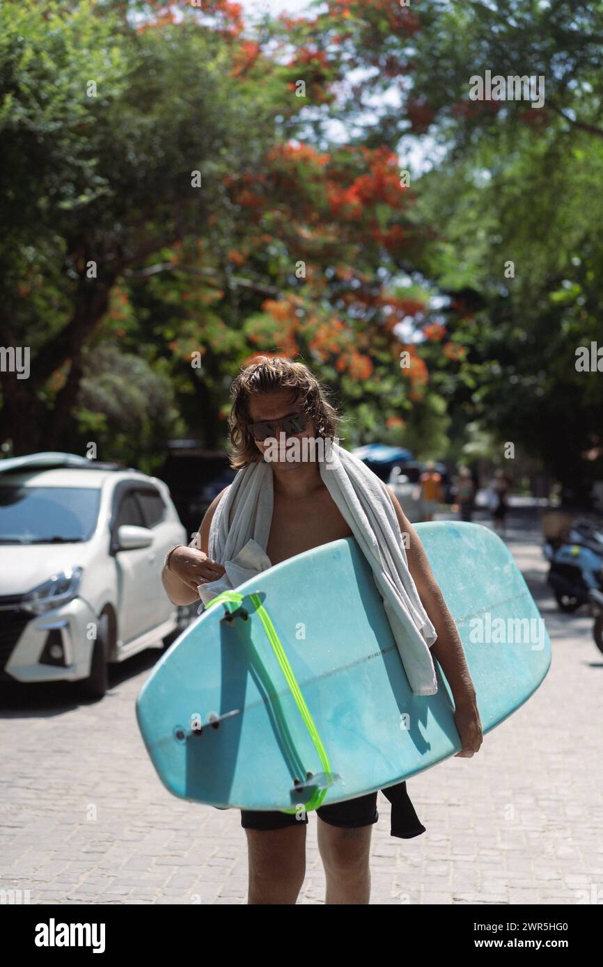 Uomo surfista con lunghi capelli sbiancati con una tavola da surf. Foto Stock