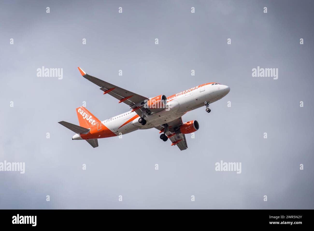 Un aeroplano easyJet, dipinto in sorprendenti colori arancio e bianco, si libra attraverso la vasta distesa del cielo blu Foto Stock