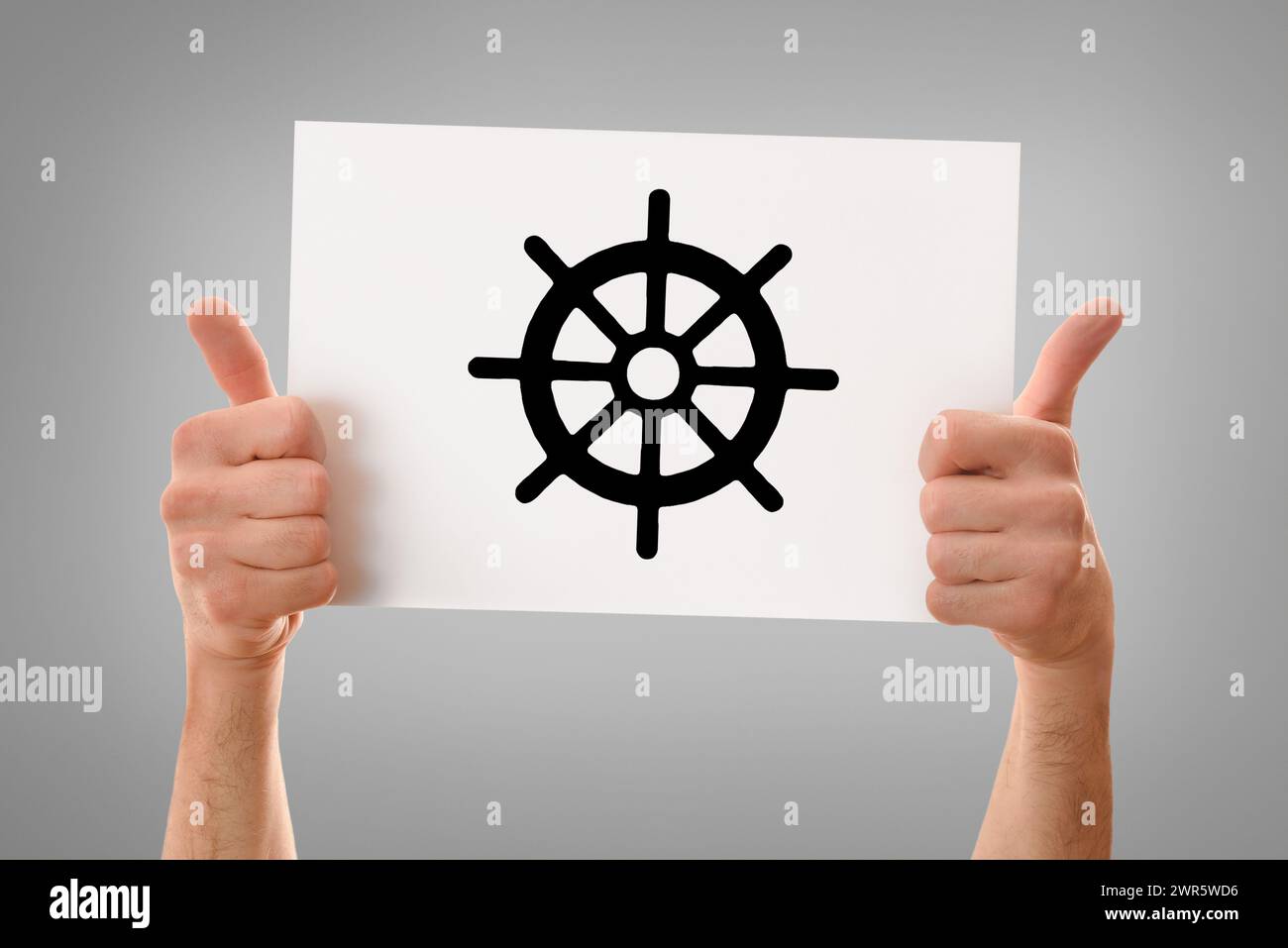 Mani di un uomo religioso con un cartello che regge un poster bianco disegnato da una ruota di dharma, sfondo grigio isolato Foto Stock