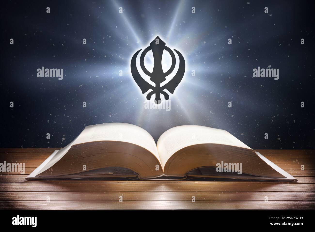 Libro aperto su tavolo in legno e simbolo sikh con fascio di luce su sfondo scuro. Vista frontale. Foto Stock