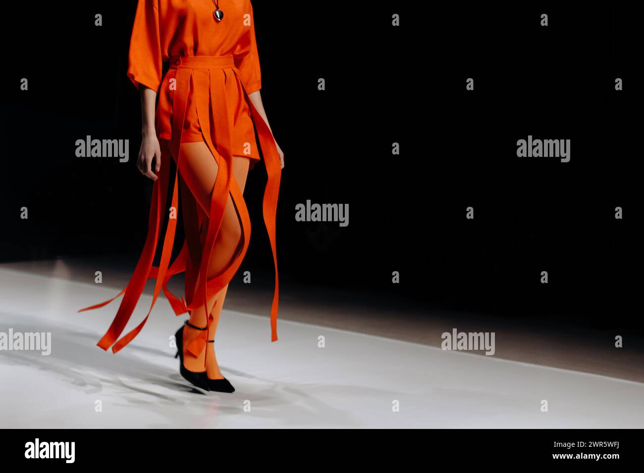 Tights e shorts firmati arancioni look alla moda da donna, modella che cammina sul podio Foto Stock