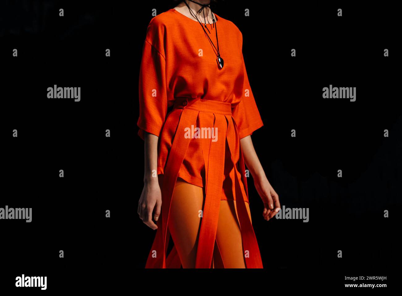 Tights e pantaloncini eleganti da donna arancioni, blusa e pantaloncini firmati, modello alla moda che cammina su sfondo nero Foto Stock