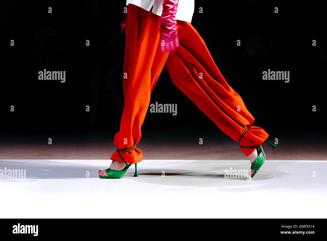 Pantaloni arancioni e tacchi alti verdi dal look trendy da donna, modella alla moda che cammina sul podio Foto Stock
