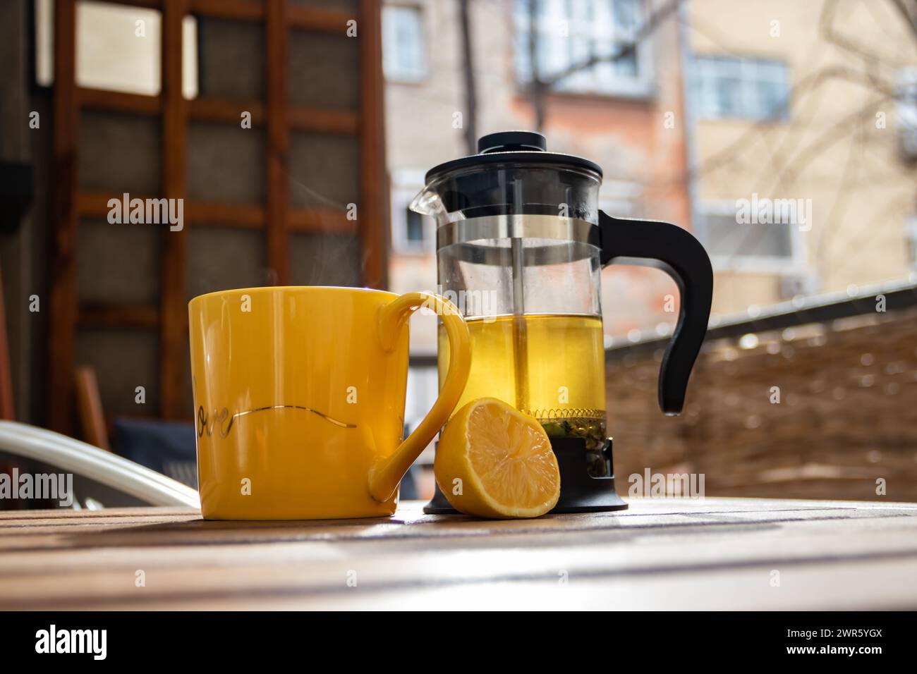 Teiera (pressa francese) con mezzo limone e teiera al tavolo di legno sul balcone, tè mattutino, aromaterapia aromatica fresca ed erboristica, tè biologico Foto Stock