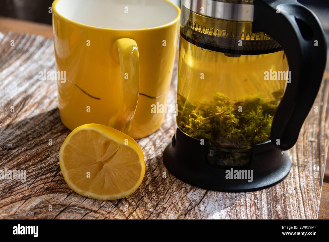 Teiera (pressa francese) con mezzo limone e teiera al tavolo di legno sul balcone, tè mattutino, aromaterapia aromatica fresca ed erboristica, tè biologico Foto Stock