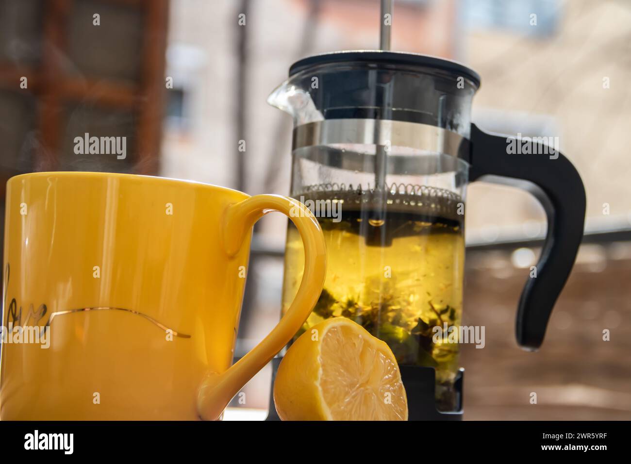 Teiera (pressa francese) con mezzo limone e teiera al tavolo di legno sul balcone, tè mattutino, aromaterapia aromatica fresca ed erboristica, tè biologico Foto Stock