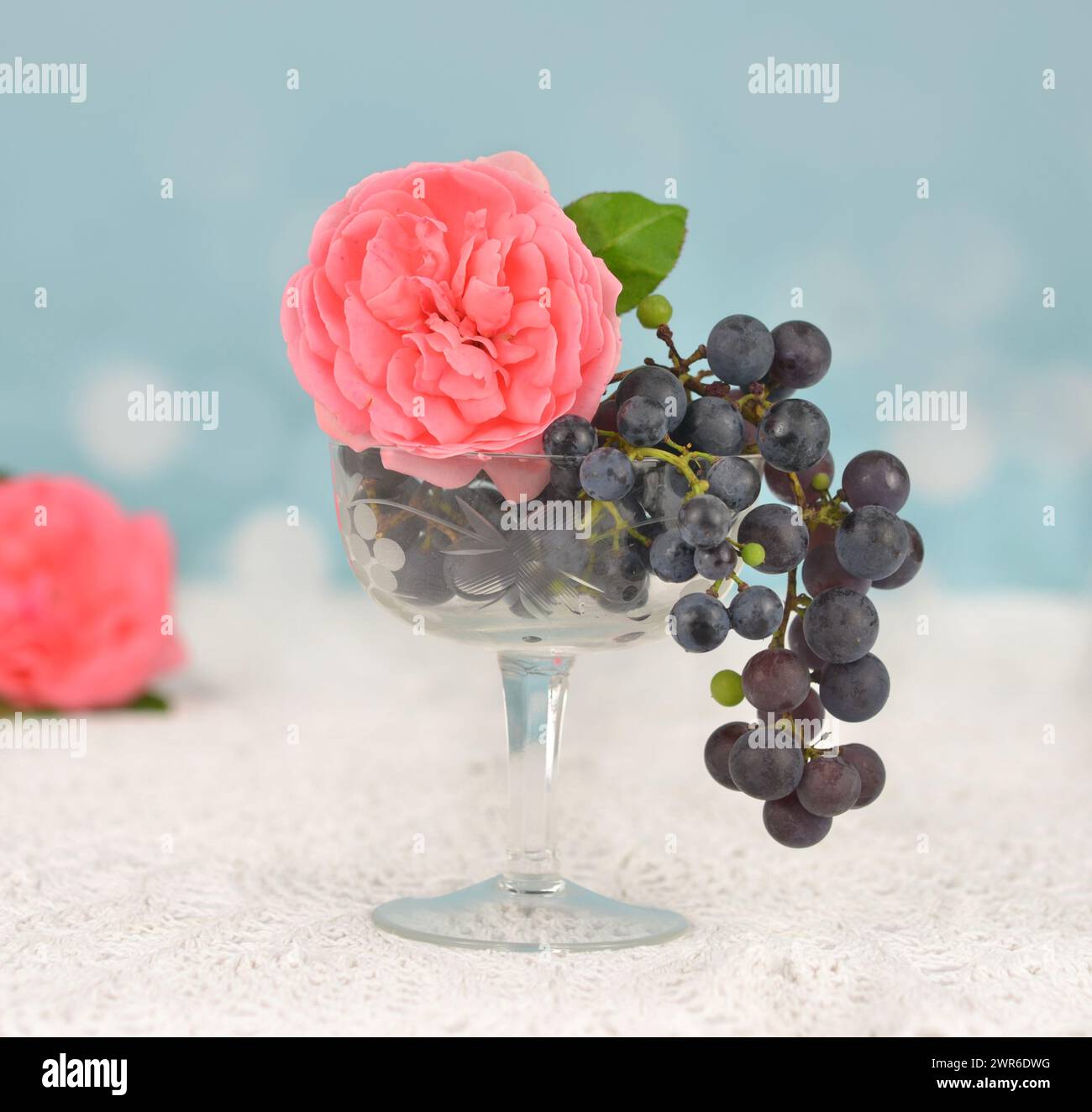 Rosa e uva in un bicchiere su un tavolo. Foto romantica. Foto Stock
