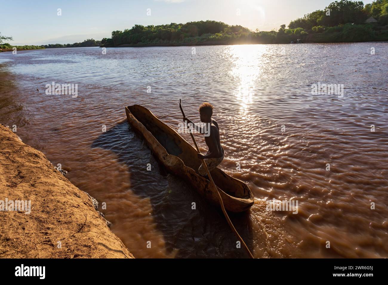 Silhouette di un uomo ferrarese che pagaia su una tradizionale barca di legno grezzo, attraversa il fiume Omo, la valle di Omo, l'Etiopia di Omorati Foto Stock