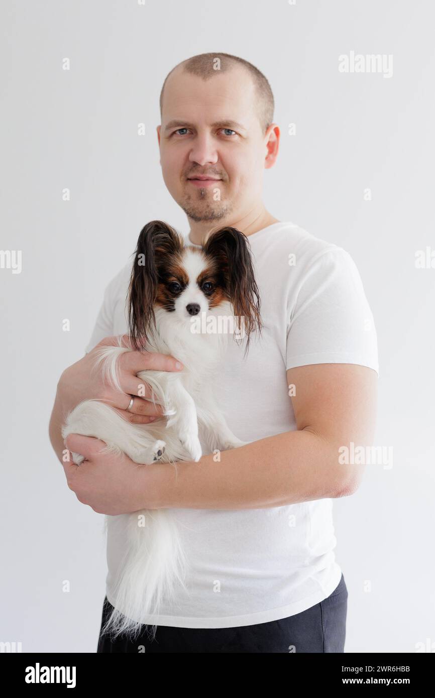 Uomo che tiene in mano il carino piccolo papillon cane sul bianco Foto Stock