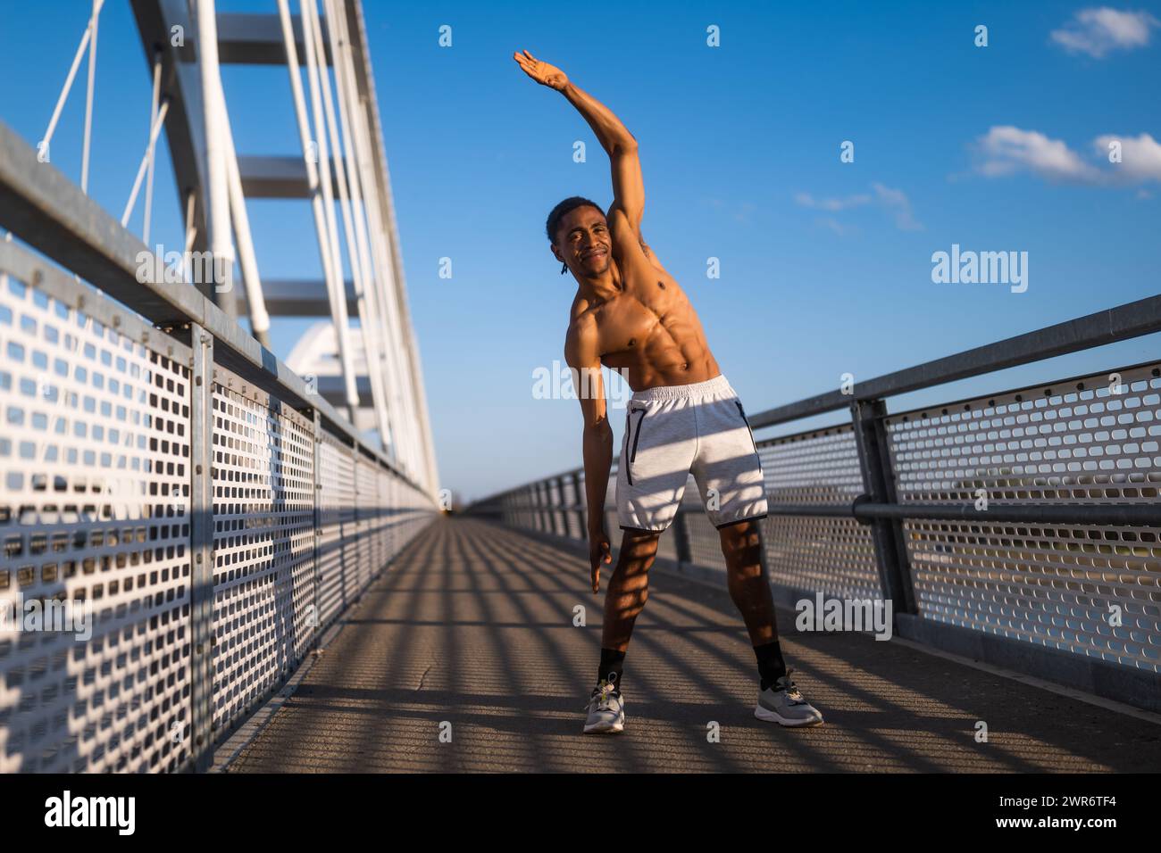 Il giovane afroamericano si sta esercitando sul ponte della città. Sta allungando il suo corpo. Foto Stock