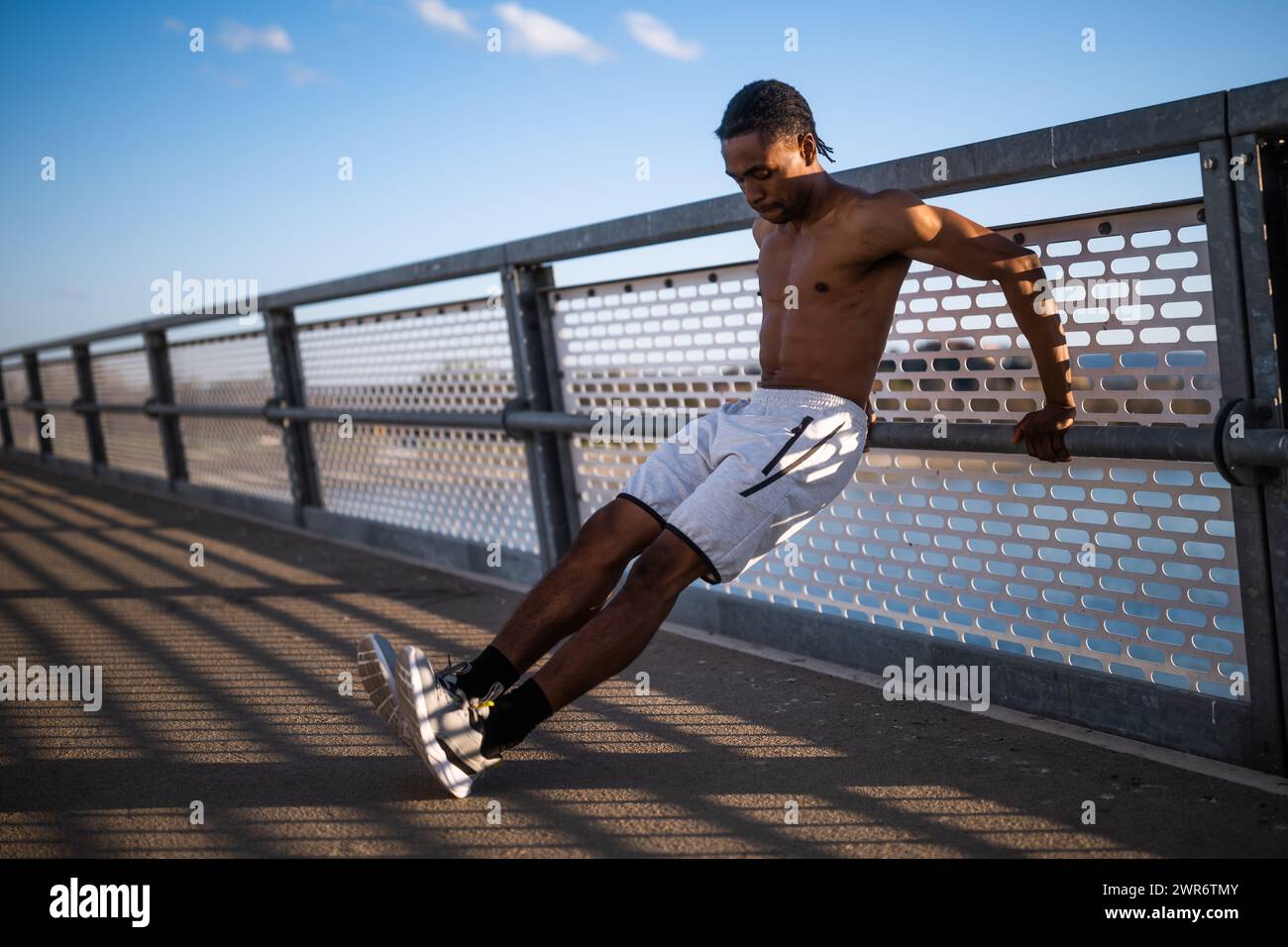 Il giovane afroamericano si sta esercitando sul ponte della città. Sta facendo push-up invertiti. Foto Stock