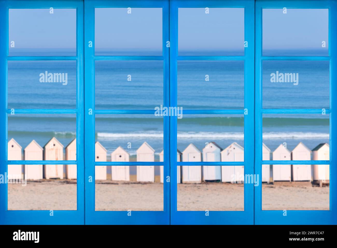 Finestra blu con vista su una spiaggia con cabine bianche d'epoca Foto Stock