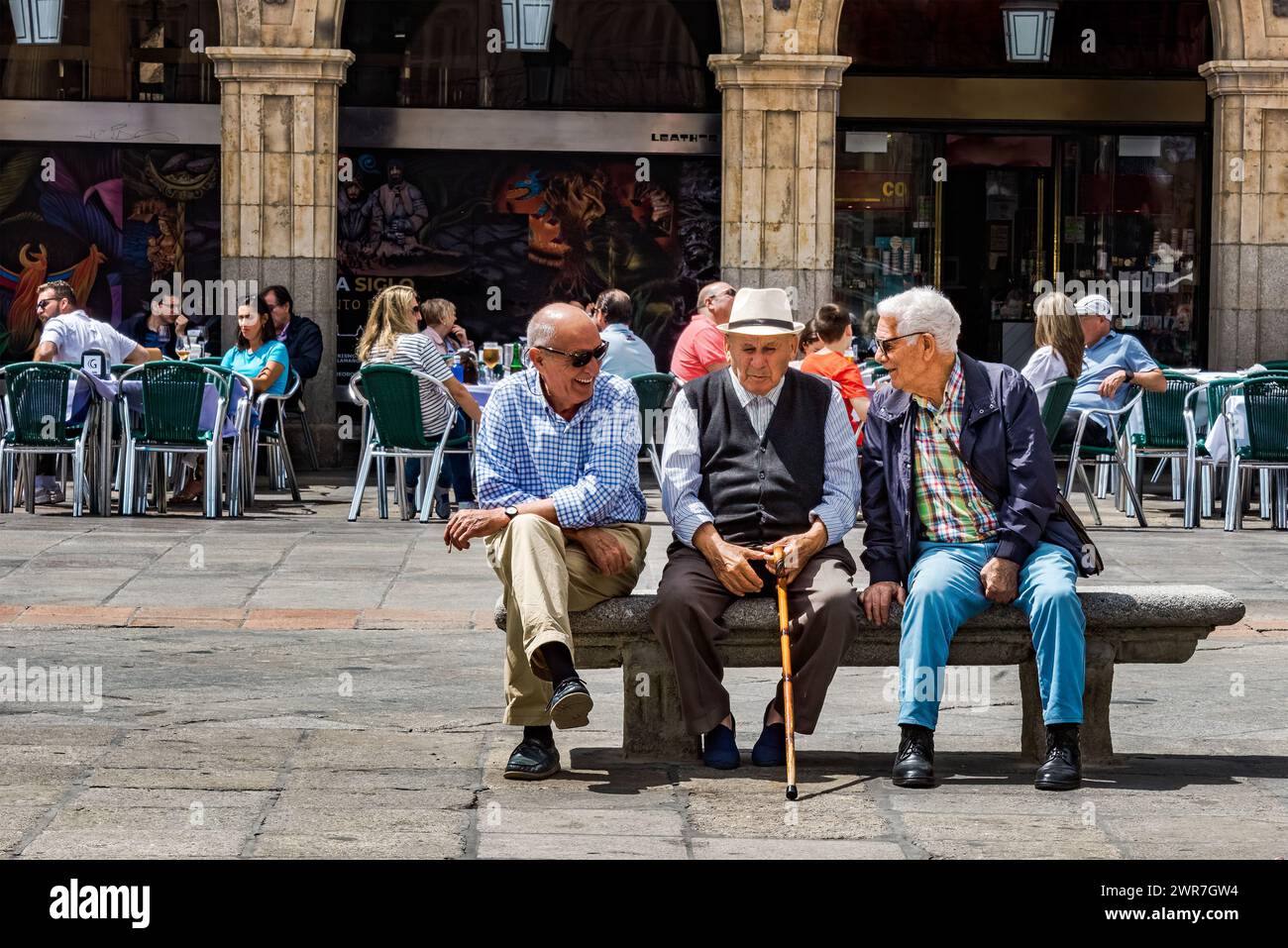 Salamanca, Spagna, 10 giugno 2023: Tre anziani sedevano su una panchina nel mezzo di Plaza Mayor, godevano di una calda giornata estiva mentre facevano una felice conversazione. Foto Stock