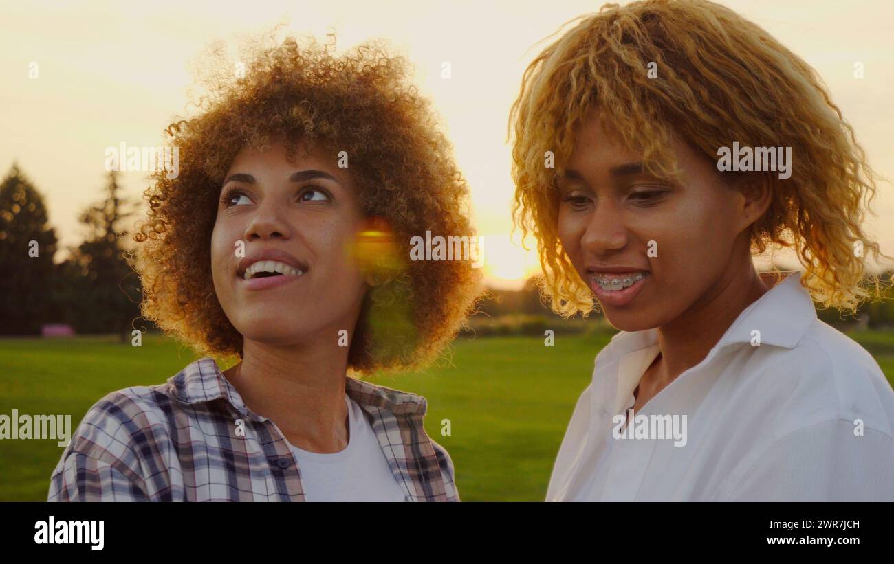 Felice e multirazziale, giovani afro Woman della generazione Z, sorelle con capelli afro, che trascorrono una giornata insieme nella natura al tramonto Foto Stock