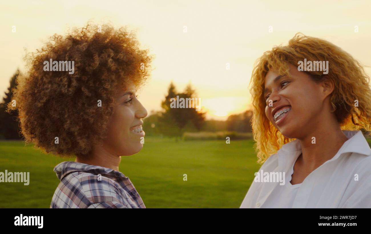 Felice e multirazziale, giovani afro Woman della generazione Z, sorelle con capelli afro, che trascorrono una giornata insieme nella natura al tramonto Foto Stock