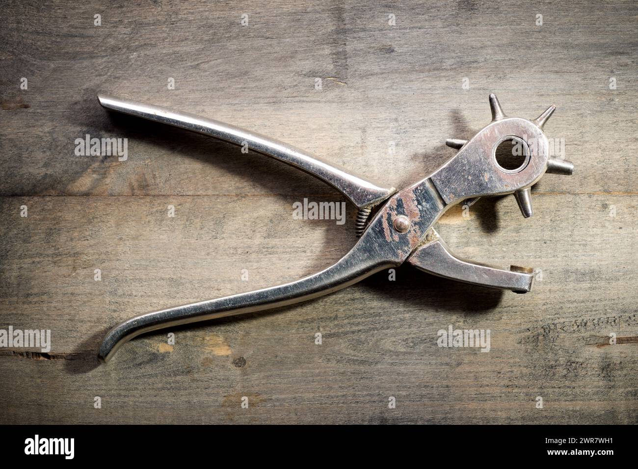 Primo piano di un utensile per praticare fori in pelle su un banco da lavoro in legno. Foto Stock