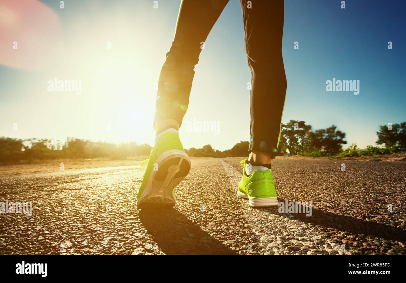 Il giovane atleta delle sneakers fa l'allenamento estivo mattutino e gli esercizi. Corsa in movimento primo piano sullo sfondo del sole nascente. Sport e guarigione Foto Stock