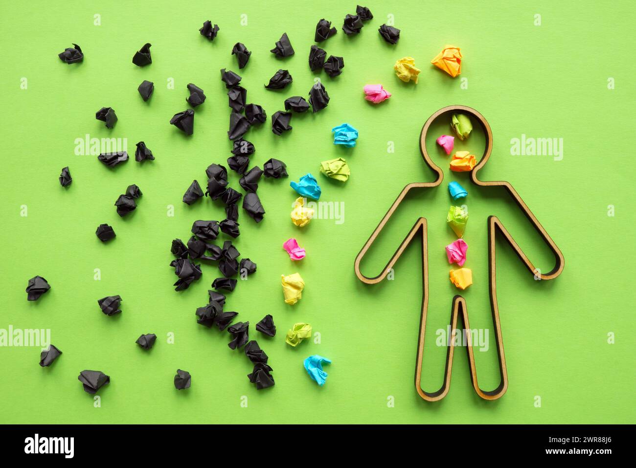 Concetto di gestione della resilienza e della negatività. Palle di carta nera circondano la statuetta con quelle colorate. Foto Stock