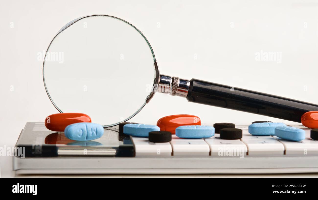 Una lente d'ingrandimento su una calcolatrice con tavolette su sfondo bianco. Una foto concettuale. Un luogo da copiare. Foto Stock