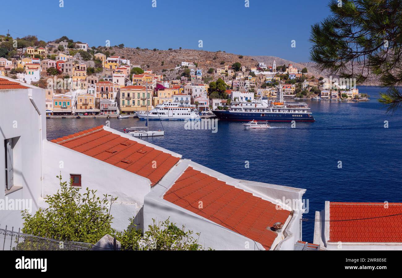 Vista delle case tradizionali colorate e delle barche da pesca nel villaggio di pescatori Symi in una giornata di sole. Grecia. Dodecaneso. Foto Stock