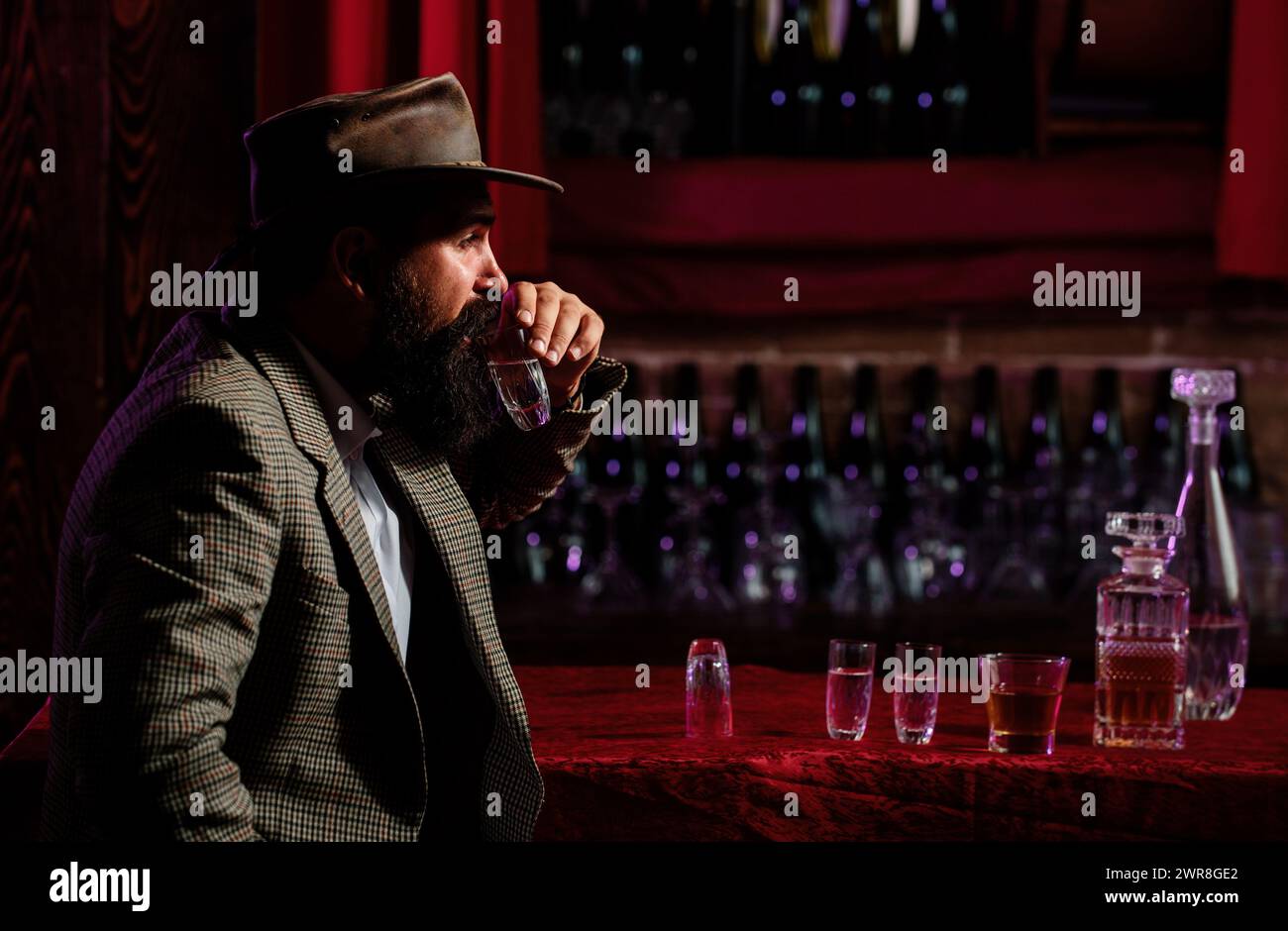 Uomo lavoratore vintage con barba lunga che tiene il whiskey. Seduto al bar. Foto Stock